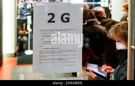 Hamburg, Germany. 14th Nov, 2021. Visitors to a performance at the Hamburger Kammerspiele pass a notice at the entrance pointing out the 2G rules now in force at the theatre. As of November 14, 2021, the Altonaer Theater and the Harburger Theater will also switch to 2G operation with reduced seating capacity Credit: Markus Scholz/dpa/Alamy Live News Stock Photo