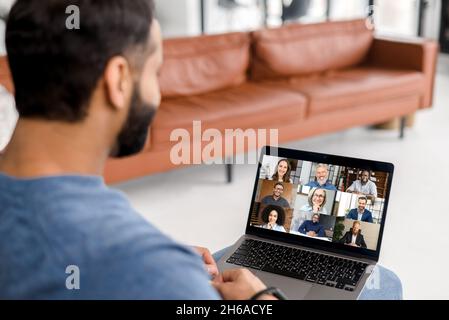 Virtual conference, online meeting. Indian man using computer app for communicating with many people at same time together. Back view. Video call with diverse employees Stock Photo