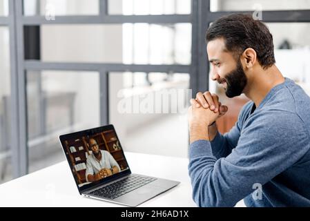 Two diverse male colleagues taking part in video meeting. Multiracial business partners involved virtual conference. Back view male Indian student takes an online language classes from African teacher Stock Photo