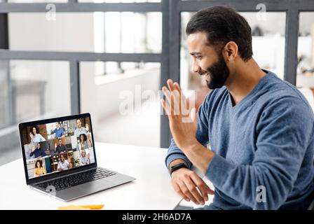Brainstorm, online video meeting, virtual conference with multi ethnic coworkers, employee, colleagues. View over shoulder of Indian guy on a screen with profiles of diverse people Stock Photo