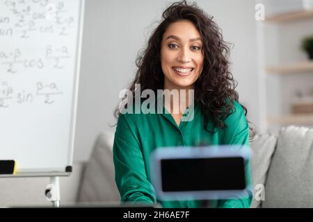 Excited young teacher making online presentation recording video lecture on cellphone. Female tutor talking on webcam, live broadcast streaming on sma Stock Photo