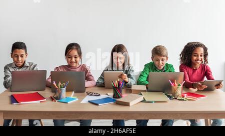 Multicultural School Children Using Laptop Computers Learning Sitting At Desk In Modern Classroom Indoors. Happy Diverse Schoolgirls And Schoolboys Br Stock Photo