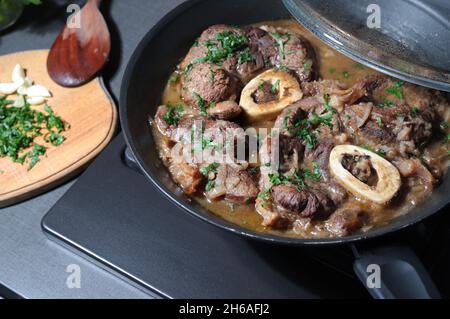 Braised veal steak Ossobuco alla Milanese with herbs in a pan. Italian cuisine. Close-up. Stock Photo