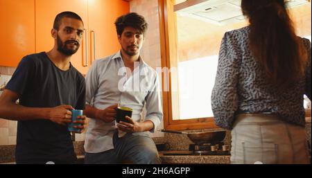 Three Indian friends talking while drinking coffee in the kitchen Stock Photo