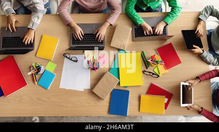 Top-View Of School Kids Using Laptop Computers Sitting At One Desk With Bright Copybooks and Supplies Indoor. Children Browsing Internet Learning Toge Stock Photo