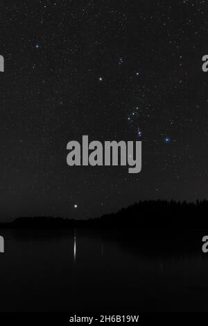 Orion constellation and Sirius star above frozen lake on a cold winter night Stock Photo