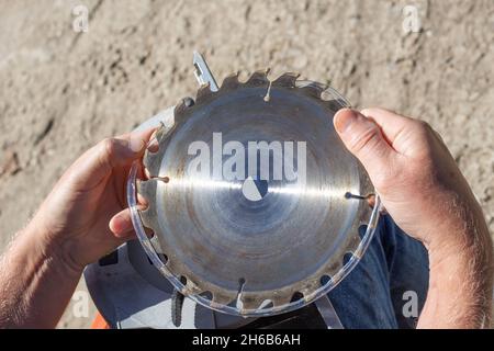 a man removes the plastic protection from the saw blade teeth on a circular miter saw for installation and replacement. Stock Photo