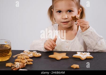 Child cooking and eating home made gingerbread cookies, stars, man. Happy toddler girl celebrated Christmas eve at home, Kid decorating pastry with Stock Photo