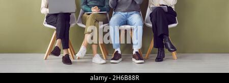 Legs of four job applicants sitting on chairs in hallway waiting in line for interview. Stock Photo
