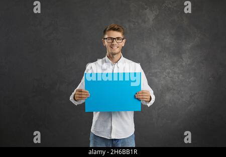 Portrait of a smiling young man showing a blank sheet of paper with space for text. Stock Photo
