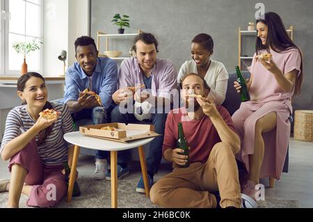 Group of happy diverse friends eating pizza, drinking beer and watching soccer on TV Stock Photo