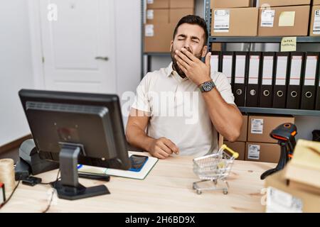 Handsome hispanic man working at small business commerce bored yawning tired covering mouth with hand. restless and sleepiness. Stock Photo