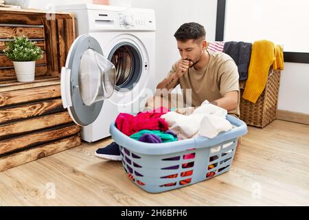 Young handsome man putting dirty laundry into washing machine feeling unwell and coughing as symptom for cold or bronchitis. health care concept. Stock Photo