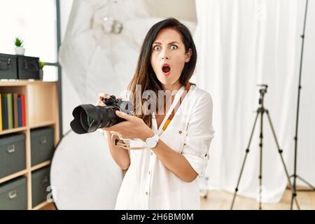 Beautiful caucasian woman working as photographer at photography studio in shock face, looking skeptical and sarcastic, surprised with open mouth Stock Photo