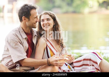 Portrait of happy young couple enjoying romantic picnic by water outdoors, copy space Stock Photo