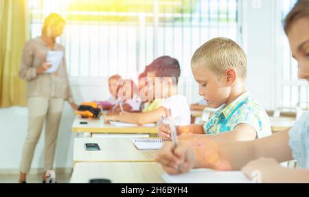 Focused tween boy writing exercises in classroom during lesson Stock Photo