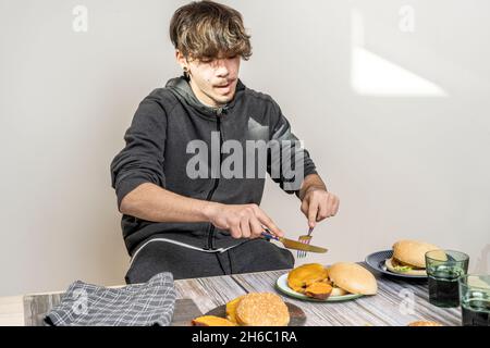 Young man sitting at the table bingeing on hamburgers