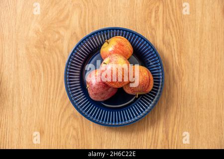 Delicious ripe red apples on blue plate seen from the top on oak background Stock Photo