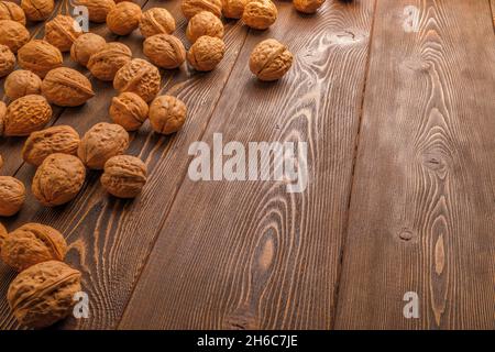 many walnuts with shells randomly scattered on brown wooden surface with copy space at right side of picture Stock Photo
