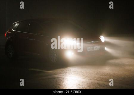 alone red Ford car moving on empty night foggy road. Stock Photo