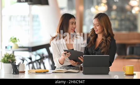 Businesswomen discussing work in office. Happy two colleagues friends working together in modern workplace. Stock Photo