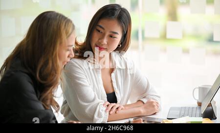 Close-up, Motivated and friendly woman sat closely listening to her colleague explain the marketing concepts at workplace. Stock Photo