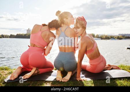 Happy women in fitness clothes relaxing and having fun in the park by the river. Fitness, sport, friendship and healthy lifestyle concept . Group of h Stock Photo