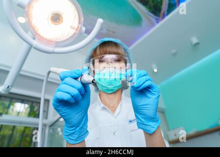 Young female dentist treating patient's teeth by filling cavity. Dentist works with professional equipment in the office of the clinic. Close up, dental care and medicine concept. Selective focus Stock Photo