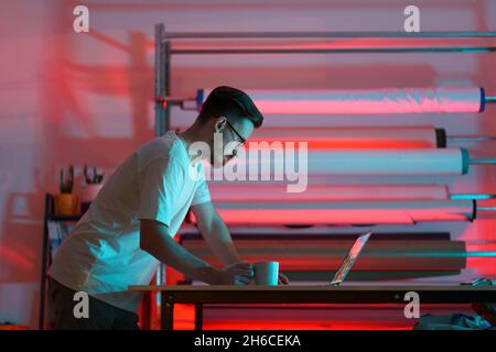Young fashion designer man in studio use laptop make orders or consult online clients about clothes Stock Photo
