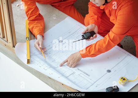 Close-up image of construction workers pointing at building blueprint and discussing detaikls Stock Photo
