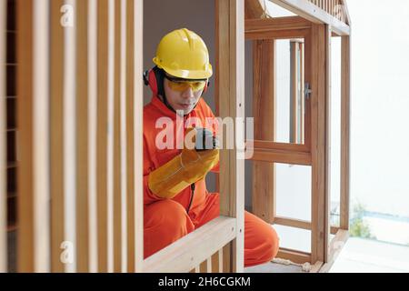 Serious builder in protective helmet, goggles and uniform building timber frame Stock Photo
