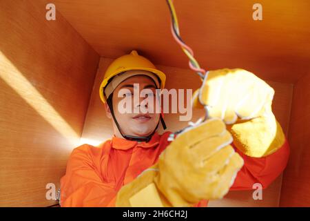 Young electrician in protective gloves connecting wires under kitchen counter Stock Photo