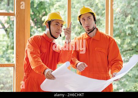 Builders with construction plan in hands discussing house walls they need to rebuild Stock Photo