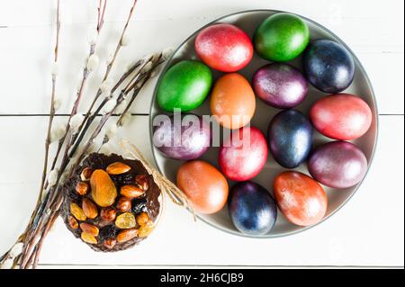top view of a large plate with Easter multi-colored eggs and willow twigs. white wooden background Stock Photo