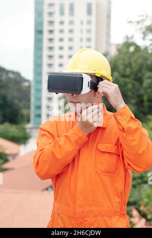 Portrait of construction worker in hardhat standing outdoors and wearing virtual reality glasses Stock Photo