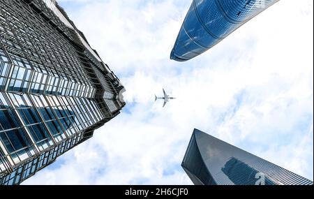 Plane flies over three modern buildings and skyscrapers of Ultra-modern Shanghai on a cloudy day, Shanghai huge international mega city in China Stock Photo
