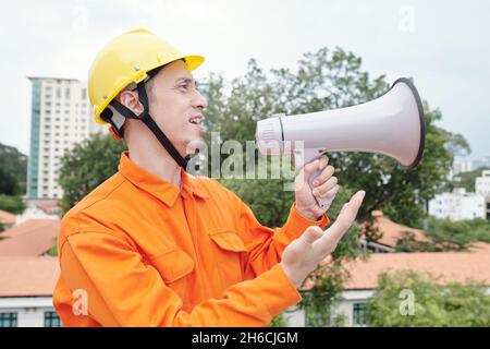 Portrait of construction site worker with loudspeaker standing on rooftop and supervising construction site Stock Photo