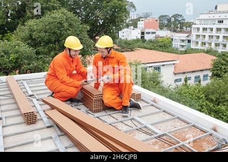 Smiling roofing contractors reading information on tablet computer before start to install wood shakes Stock Photo