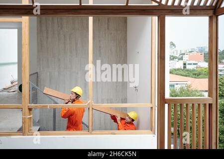 Team of construction workers carrying thick heavy board to the second floor where they are laying flooring Stock Photo