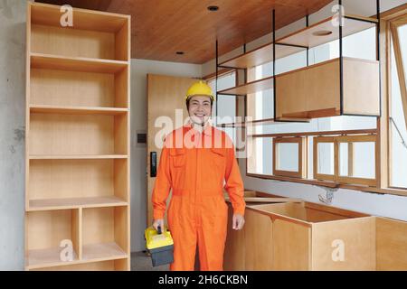 Happy Asian carpenter with toolbox standing in apartment he came to install kitchen counter Stock Photo