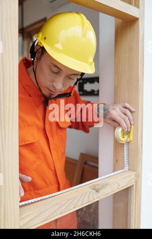 Serious construction worker measuring wooden window frame with tape measure Stock Photo