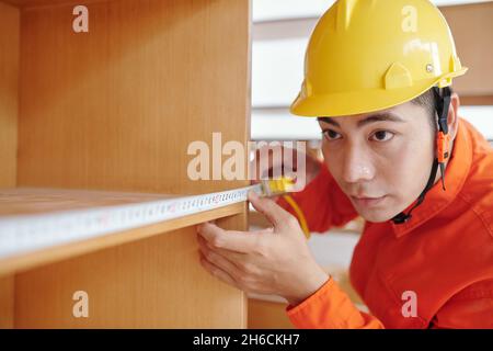Concentrated workman measuring shelves width of wooden bookcase Stock Photo