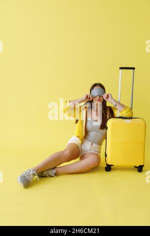 Charming woman in sleep mask sitting near travel bag Stock Photo