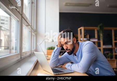 Depressed young African-american teacher using laptop indoors in staffroom. Stock Photo