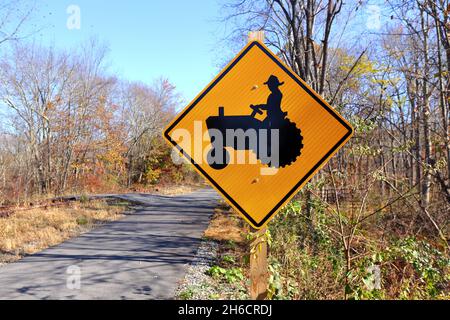 A farm vehicle traffic warning sign on a country road. Farm equipment crossing and farm machinery traffic warning sign. Stock Photo
