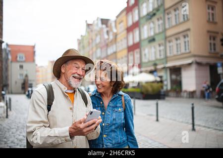 Portrait of happy senior couple tourists using smartphone outdoors in historic town Stock Photo