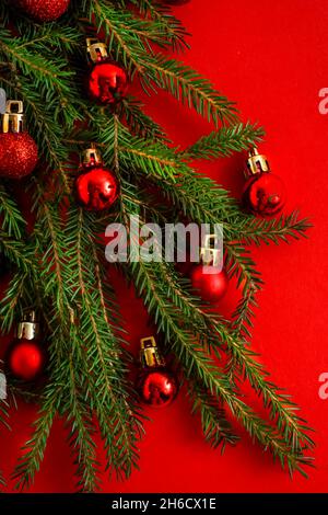Christmas tree made of green coniferous branches on a red background. Christmas background with place for text. Christmas holiday concept. Ball toys. Stock Photo