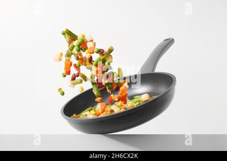 Fresh vegetables fly in a pan on a white background. Cooking with various chopped vegetables in a pan. The concept of healthy eating and diet. Stock Photo