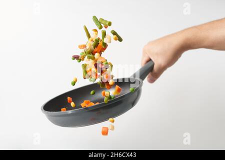 Fresh vegetables fly in a pan on a white background. Cooking with various chopped vegetables in a pan. The concept of healthy eating and diet. Stock Photo