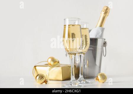 New Year champagne in wineglasses and bottle in bucket decorated festive Christmas gold baubles on white background. Close up. Holiday greeting card w Stock Photo